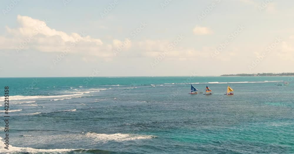 Sailboats floating leisurely on ocean waters off the coast of tropical paradise Porto de Galinhas, Brazil. Wide shot, push in. Sailboats floating leisurely on ocean waters off the coast of tropical paradise Porto de Galinhas, Brazil. Wide shot, push in.