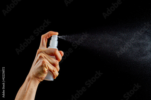 A caucasian woman is holding a small plastic spray top fine mist sprayer bottle and pressing the top button to spray colorless liquid. Versatile image with copy space for cosmetics, cleaning, physics. photo