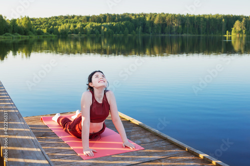 girl doing yoga on wooden pier by lake in summer