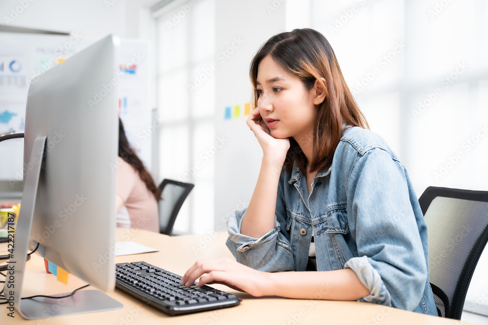 Young asian beautiful woman working on computer at workplace with a business team group Young asian beautiful woman working on computer at workplace with a business team group
