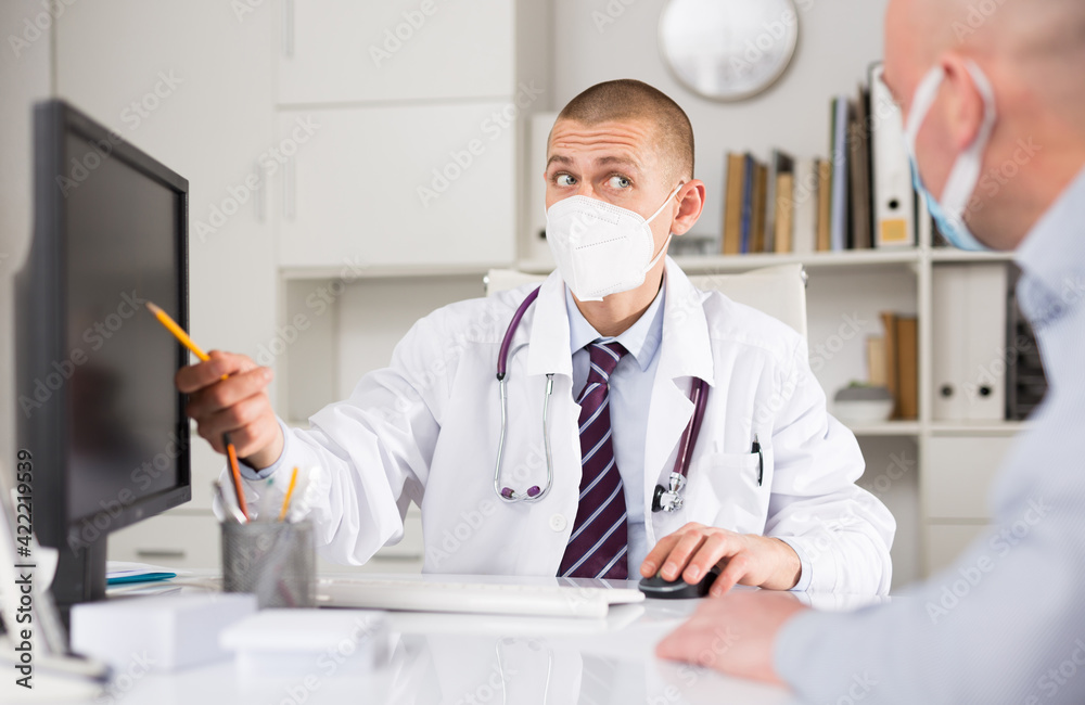 Portrait of a doctor in protective mask advising a patient during an epidemic in hospital office