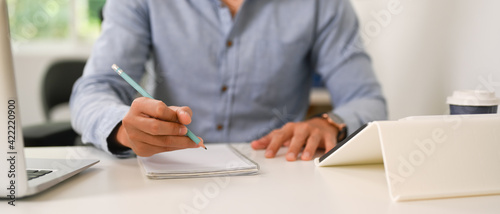 Cropped shot of businessman holding pen writing on empty notebook at office desk.