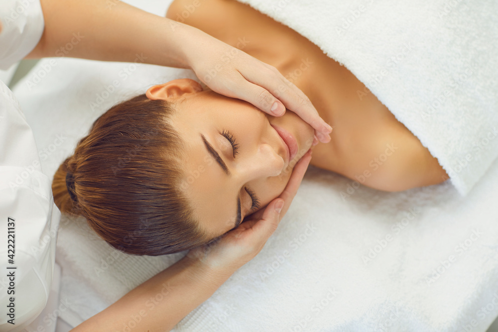 Woman enjoying procedure of facial massage from cosmetologist