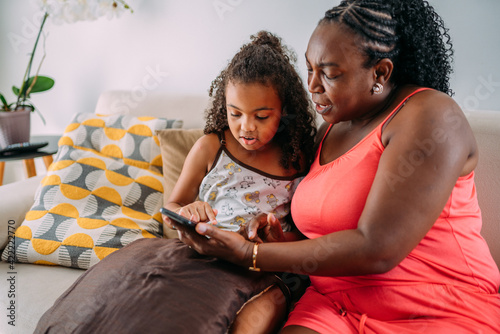 latinx grandmother using cellphone on sofa with granddaughter photo