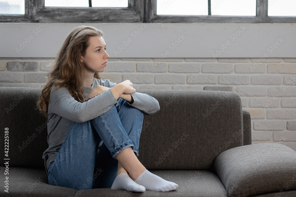 Depressed teenager girl with sad emotions and feelings sitting on the couch at home Depressed teenager girl with sad emotions and feelings sitting on the couch at home