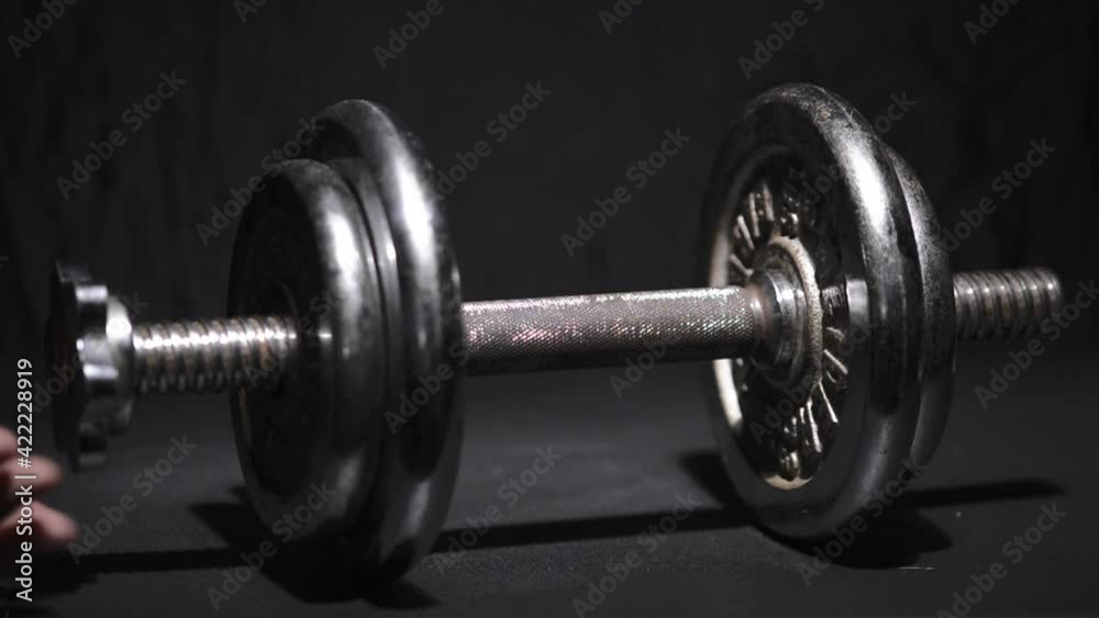 Dumbbells being loaded with plates and lifted on a dark blue background Dumbbells being loaded with plates and lifted on a dark blue background