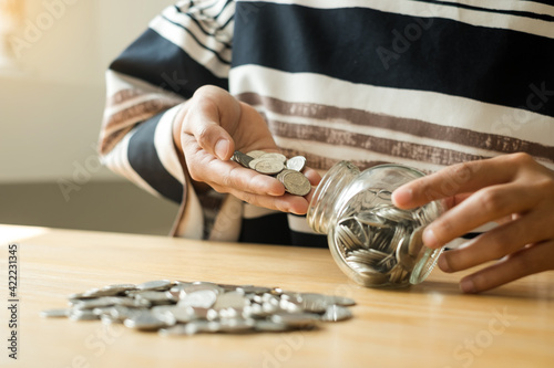 Woman's hand. Put a coin into a glass bottle with coins, saving money with coins, stepping into a successful growing business, and saving for thought in retirement. Retirement savings concept