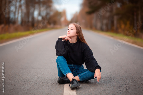 Young woman traveller in casual clothes sitting on road. Concept freedom, happy and travel. Autumn landscape