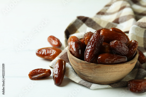 Bowl of dried dates on kitchen napkin on white wooden background