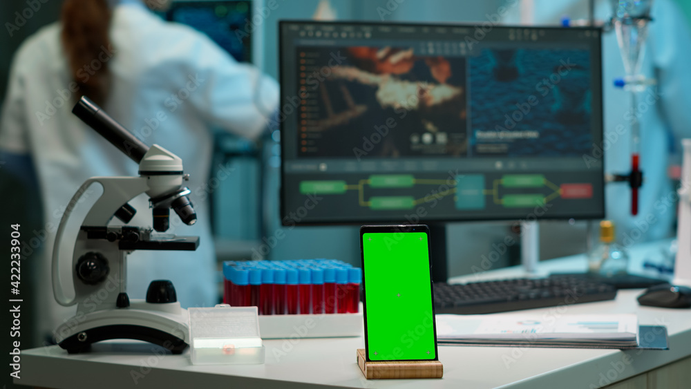 Display phone with green screen, mock up on template placed on desk in scientific lab while team of medical researcher scientists analysing virus evolution at digital monitor conducting experiment Display phone with green screen, mock up on template placed on desk in scientific lab while team of medical researcher scientists analysing virus evolution at digital monitor conducting experiment
