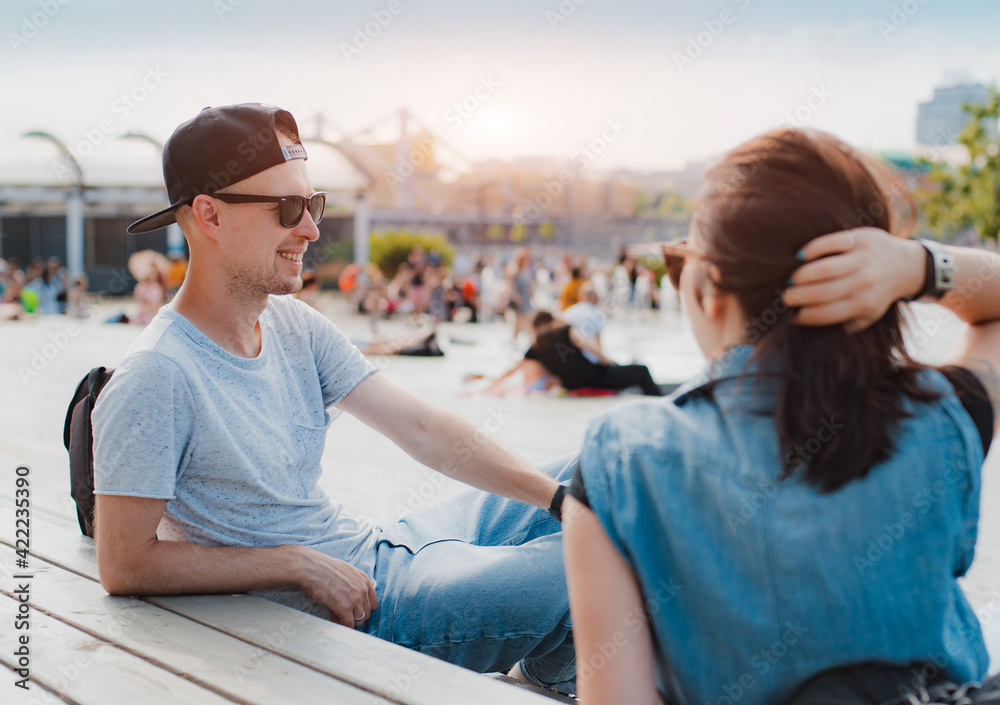 Obraz premium stylish young couple have fun chatting city square summer sunset. happy guy laughs date with girl. sunglasses, meeting, friendship, summer, hipster, cap, trend, modern youth, introduction, man woman