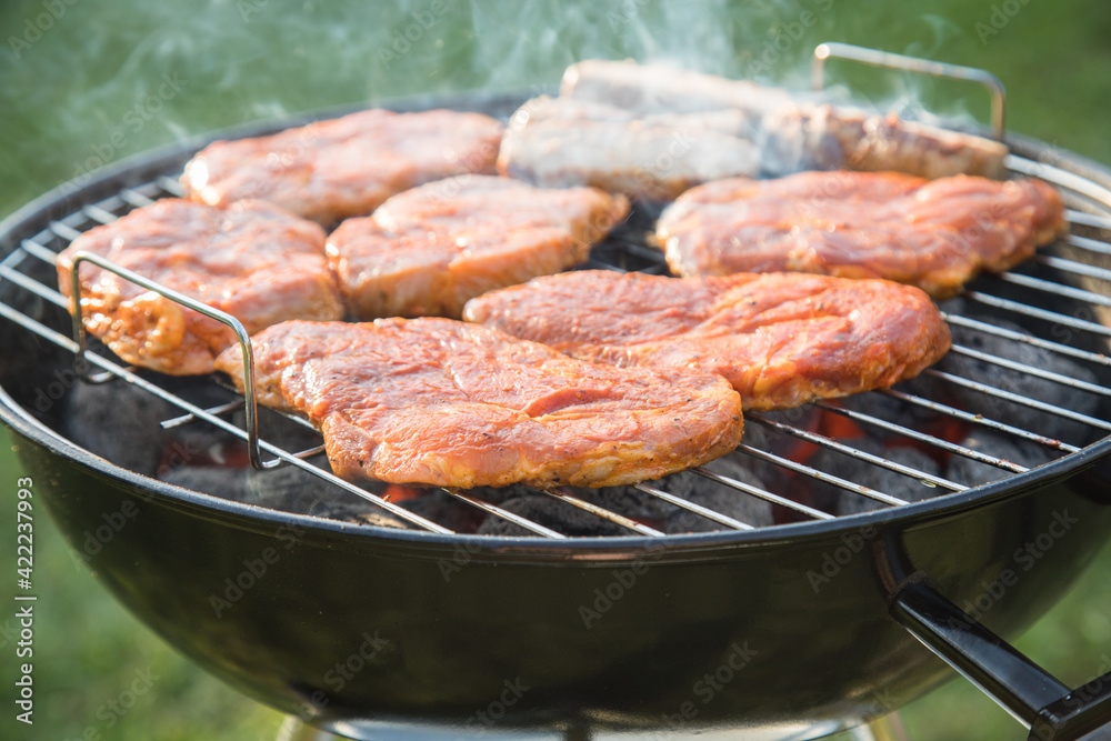 Marinierte Schweine Fleisch Nackensteaks roh grillen mit Rauch auf Holzkohle Kugelgrill im Garten an Sommer Abend