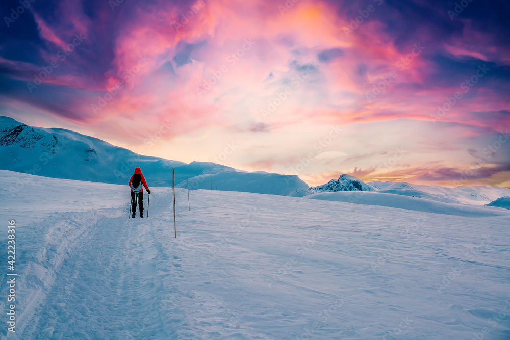 Person walking on a mountain trail in the snow in a majestic artic wilderness during sunset.