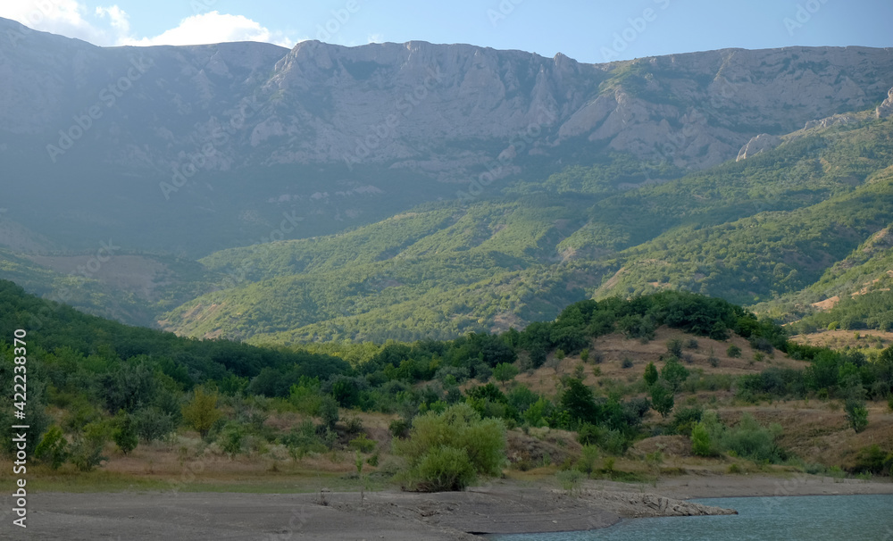 The shore of a mountain lake in the midst of inaccessible rocks, surrounded by a green forest.