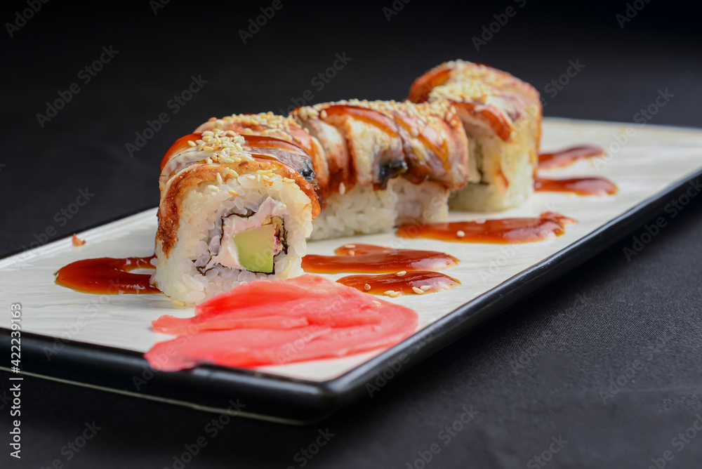 Sushi set, sushi rolls with cream cheese and eel served on a white plate over black background. Sushi set, sushi rolls with cream cheese and eel served on a white plate over black background.
