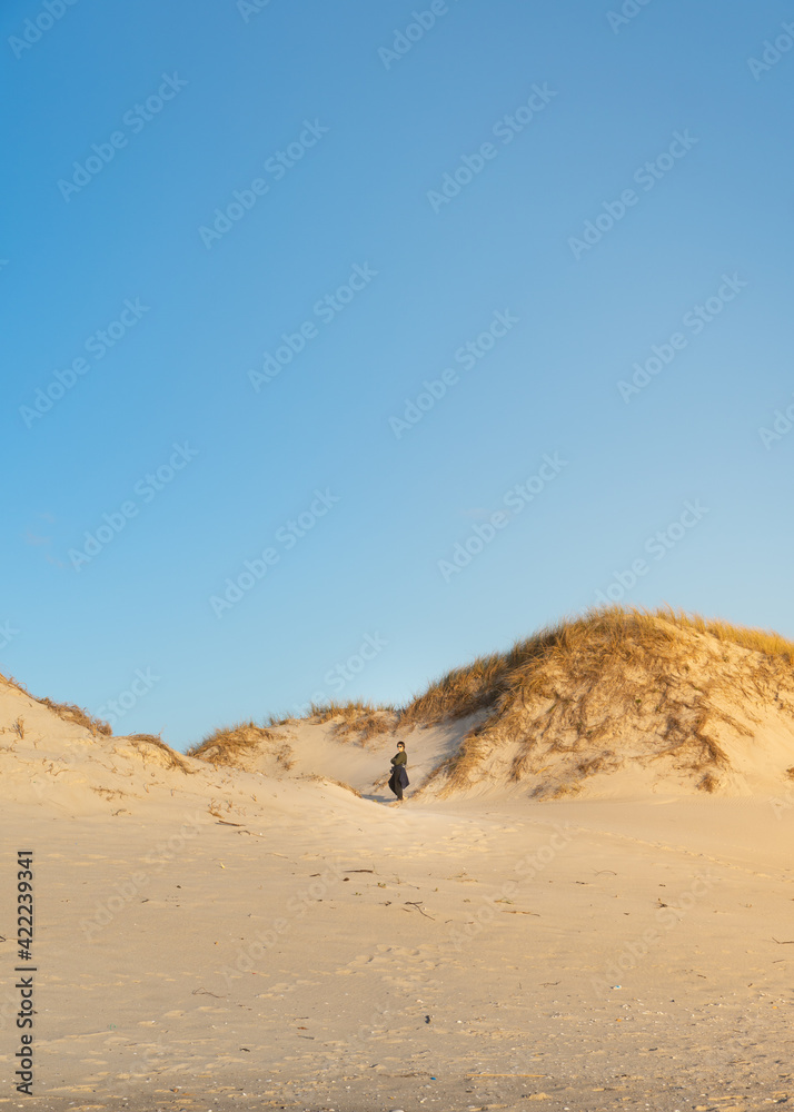 Mujer Joven caminando por el desierto, parada en medio de unas dunas con luz de atardecer