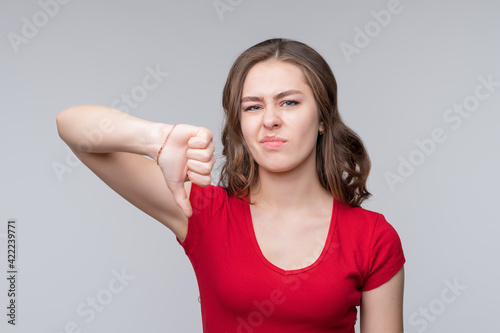 Portrait of displeased young woman showing thumb down gesture on gray background