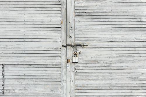 Gray wooden garage door. Metal padlock background. Peeling paint wood. Vintage rustic gate. Empty copy space grunge door texture.
