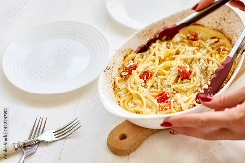 Woman hand's cooking trending viral baked tomatoes and feta with pasta, Fetapasta on a white wooden background . New, popular dinner dish, Top view, copy space.. photo