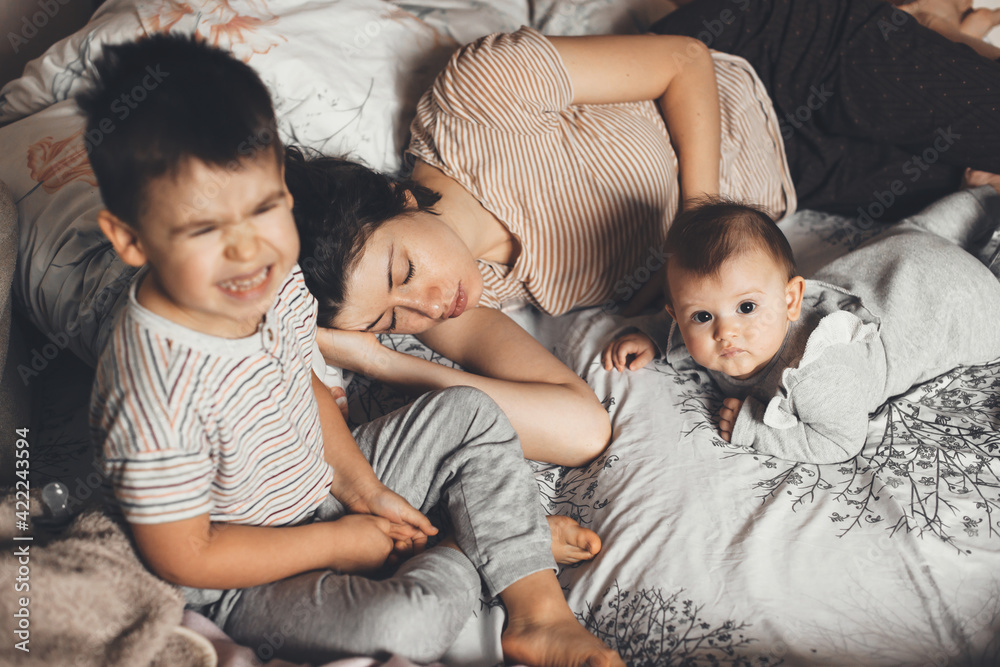 upper view photo of a tired caucasian mother sleeping in bed while her kids are making noise on couch upper view photo of a tired caucasian mother sleeping in bed while her kids are making noise on couch