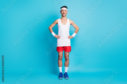 Full length photo of sporty man hold hand waist wear white singlet gumshoes isolated over blue color background