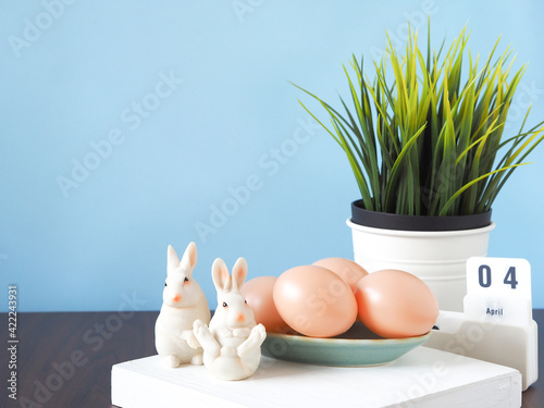 Easter eggs in turquoise plate and bunny, calendars, decorative trees with blue backdrop. Space for your text. Festive concepts. photo