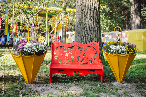 Beautiful photo zone with red bench and yellow decorative umbrellas with flowers standing in the park. Decor in the garden