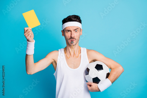 Photo of serious brown haired guy hold show yellow card football judge whistle isolated on blue color background photo