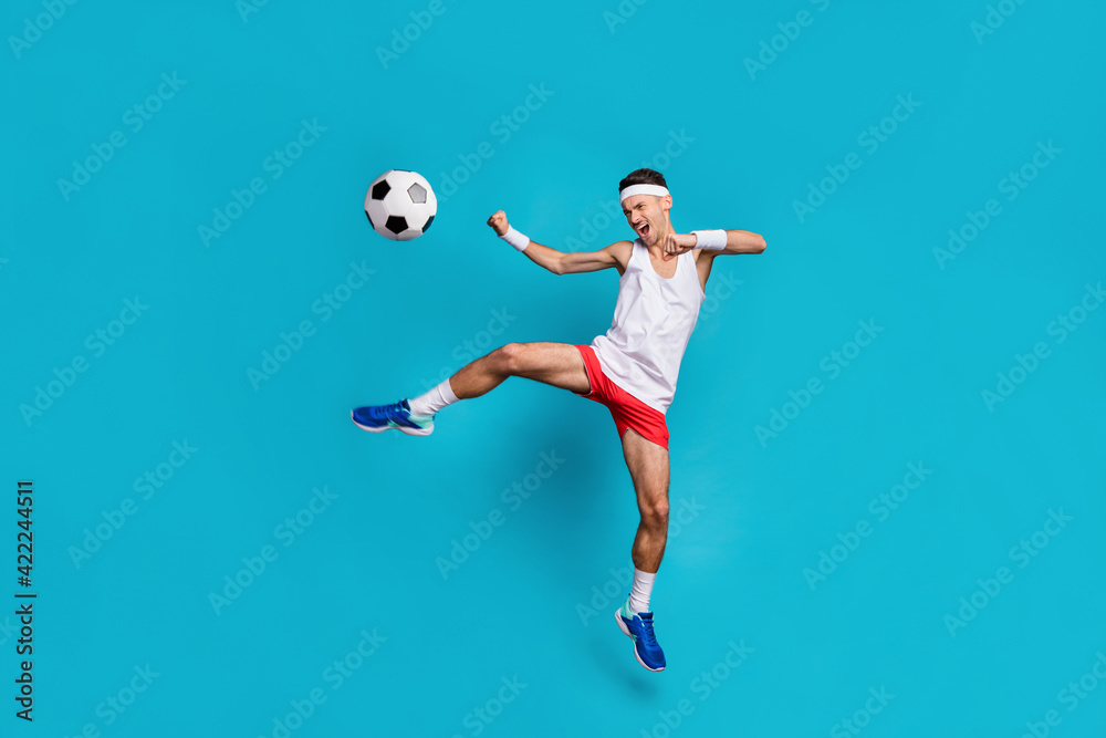 Fototapeta premium Full size portrait of young guy open mouth shout jumping leg kick ball wear long socks isolated on blue color background