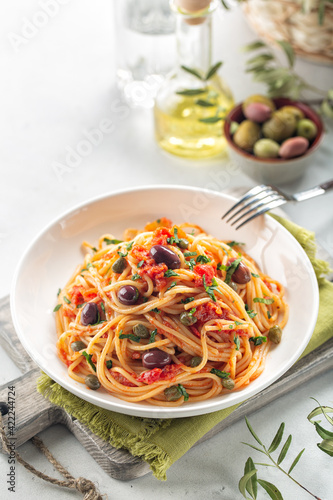 Italian lunch. Spaghetti alla puttanesca - italian pasta dish with tomatoes, olives, capers and parsley. Light background. Copy space. Vertical image.