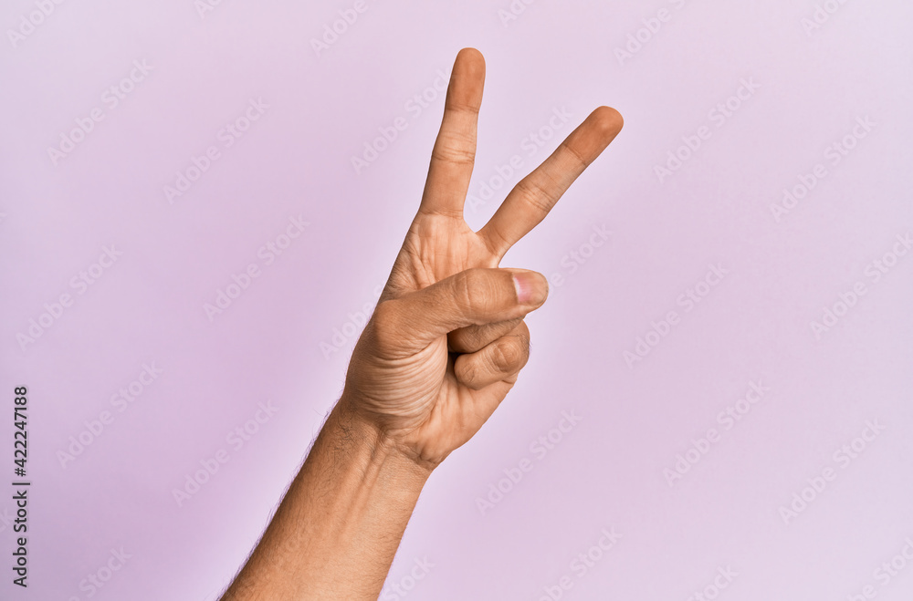 Arm and hand of caucasian young man over pink isolated background counting number 2 showing two fingers, gesturing victory and winner symbol