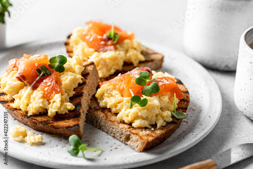 Scrambled egg sandwich with salmon on a ceramic plate on a white background, selective focus, close-up