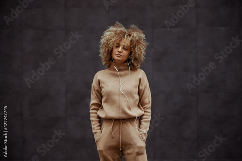 Hip hop girl in tracksuit standing with hands in her pockets and listening music. photo