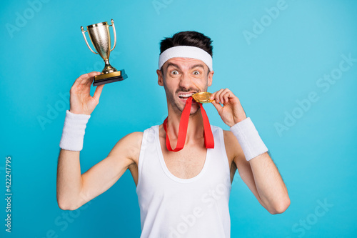 Photo of brown haired lucky man win medal golden trophy bite teeth isolated on blue color background photo