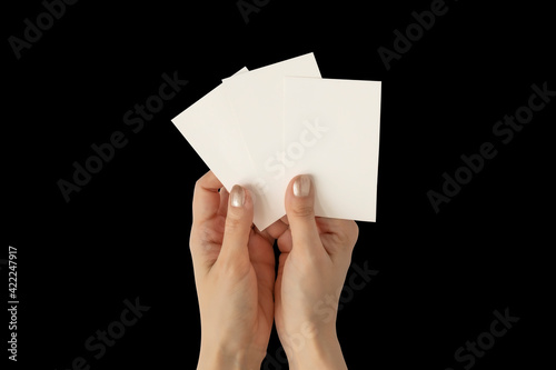 Hands of young woman with golden nail polish holding three blank business cards mockup, stationery template isolated on black background.