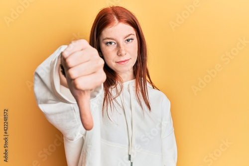 Young red head girl wearing casual sweatshirt looking unhappy and angry showing rejection and negative with thumbs down gesture. bad expression.