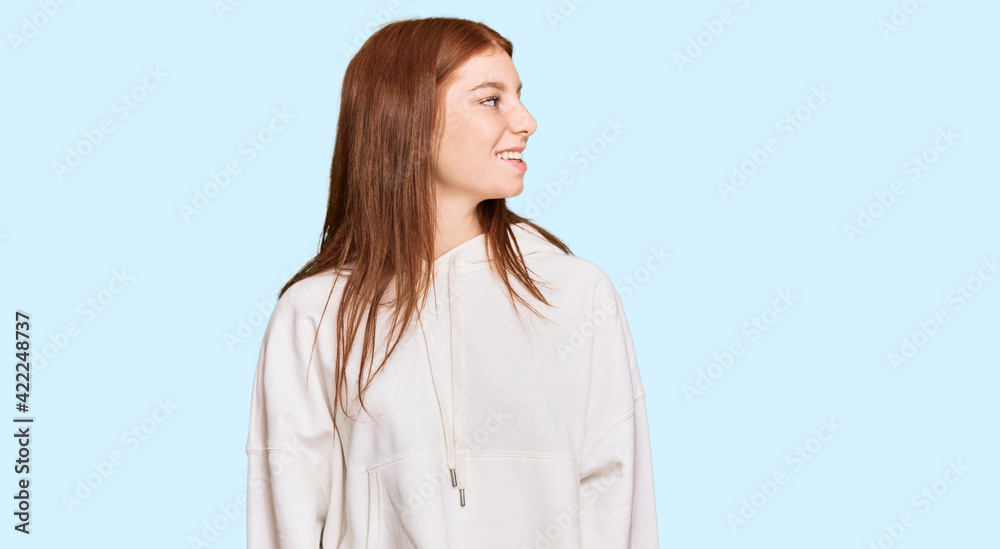 Young read head woman wearing casual sweatshirt looking away to side with smile on face, natural expression. laughing confident. Young read head woman wearing casual sweatshirt looking away to side with smile on face, natural expression. laughing confident.
