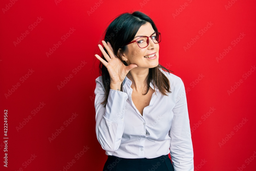 Young hispanic woman wearing business shirt and glasses smiling with hand over ear listening an hearing to rumor or gossip. deafness concept. Young hispanic woman wearing business shirt and glasses smiling with hand over ear listening an hearing to rumor or gossip. deafness concept.