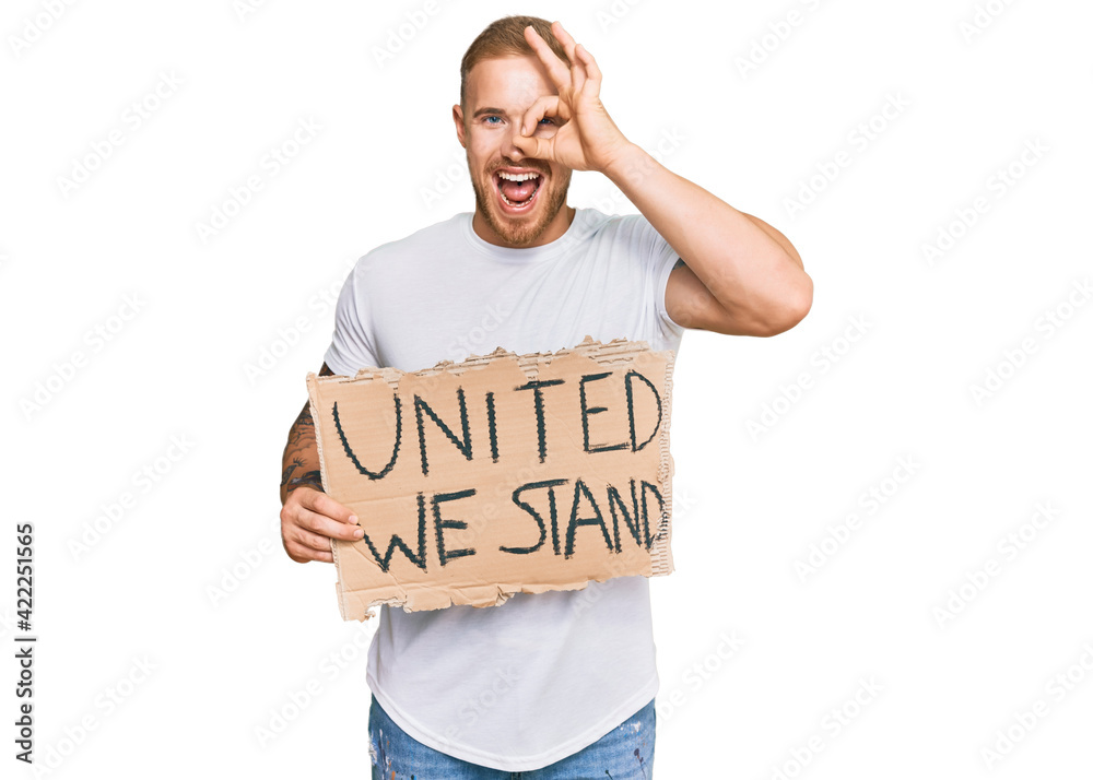 Young irish man holding united we stand banner smiling happy doing ok sign with hand on eye looking through fingers Young irish man holding united we stand banner smiling happy doing ok sign with hand on eye looking through fingers