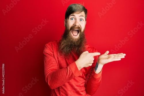 Redhead man with long beard pointing open palm with finger celebrating crazy and amazed for success with open eyes screaming excited.