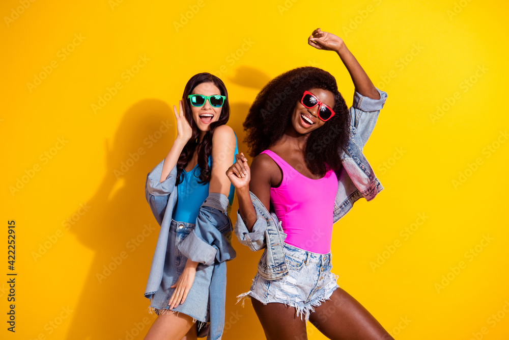 Photo of two funky cheerful ladies enjoy dance wear sunglass top jeans outfit isolated yellow color background Photo of two funky cheerful ladies enjoy dance wear sunglass top jeans outfit isolated yellow color background