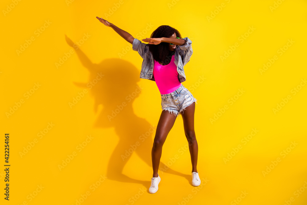 Full body photo of funky afro american lady dance dab weekend wear jeans jacket isolated on shine yellow color background Full body photo of funky afro american lady dance dab weekend wear jeans jacket isolated on shine yellow color background