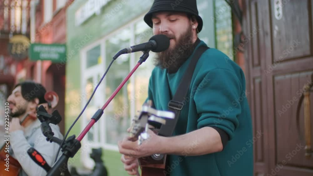 Tracking shot of street musicians with acoustic guitar and cello performing song Tracking shot of street musicians with acoustic guitar and cello performing song