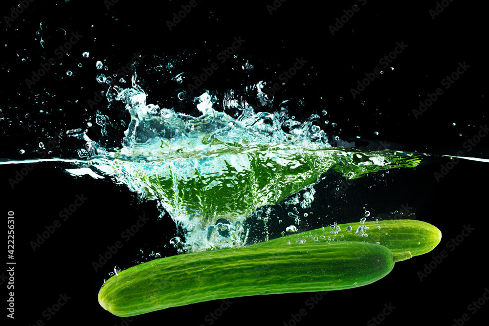 Fototapeta premium Cucumbers falling into the water with a splash againsty black background