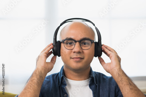 Young asian man wearing headphone and listen the music. He in living room sitting on sofa.