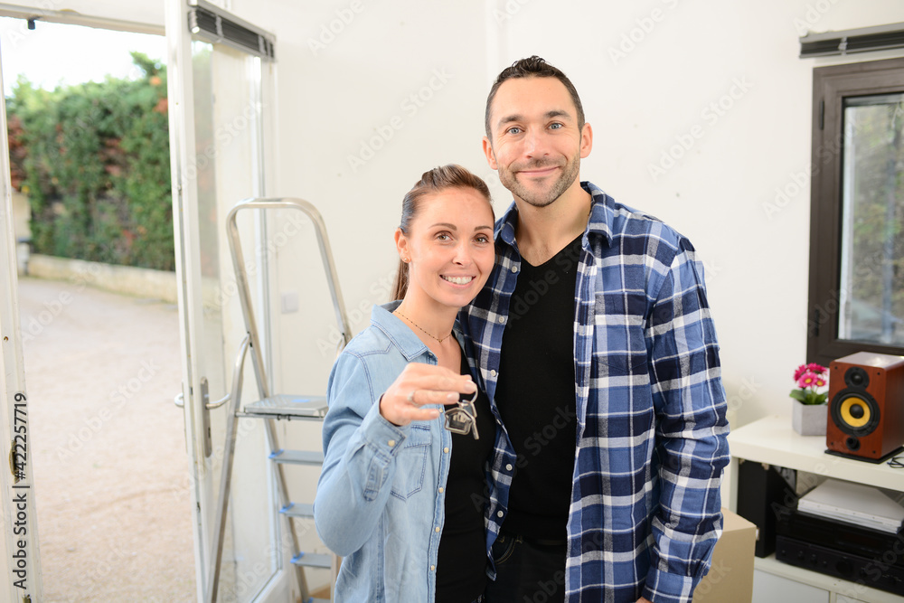 Young happy couple moving in new home and showing proudly their new house keys