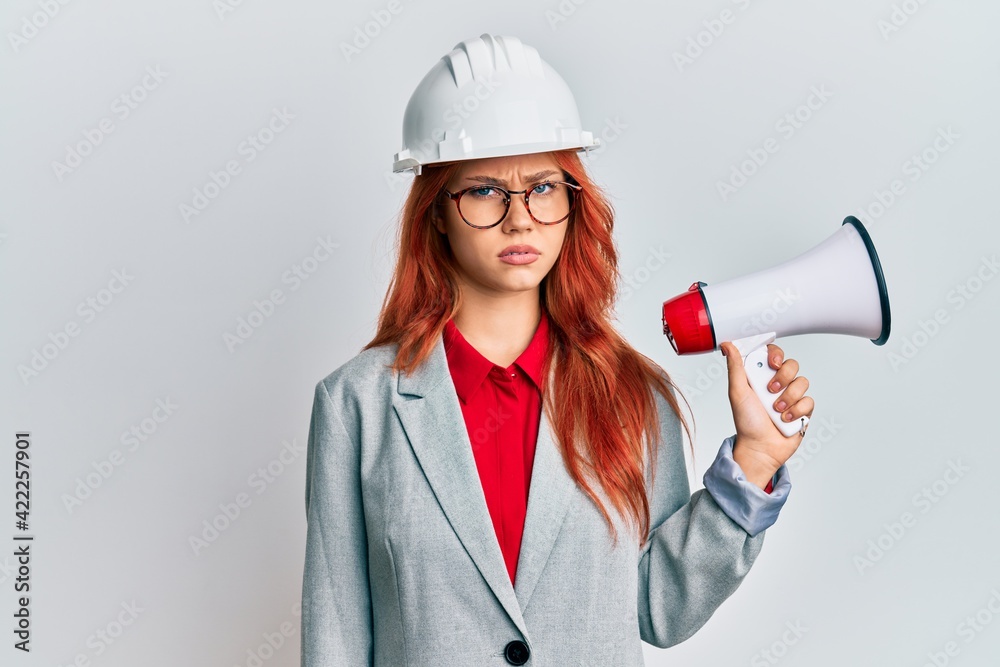 Young redhead woman wearing architect hardhat and megaphone skeptic and nervous, frowning upset because of problem. negative person. Young redhead woman wearing architect hardhat and megaphone skeptic and nervous, frowning upset because of problem. negative person.