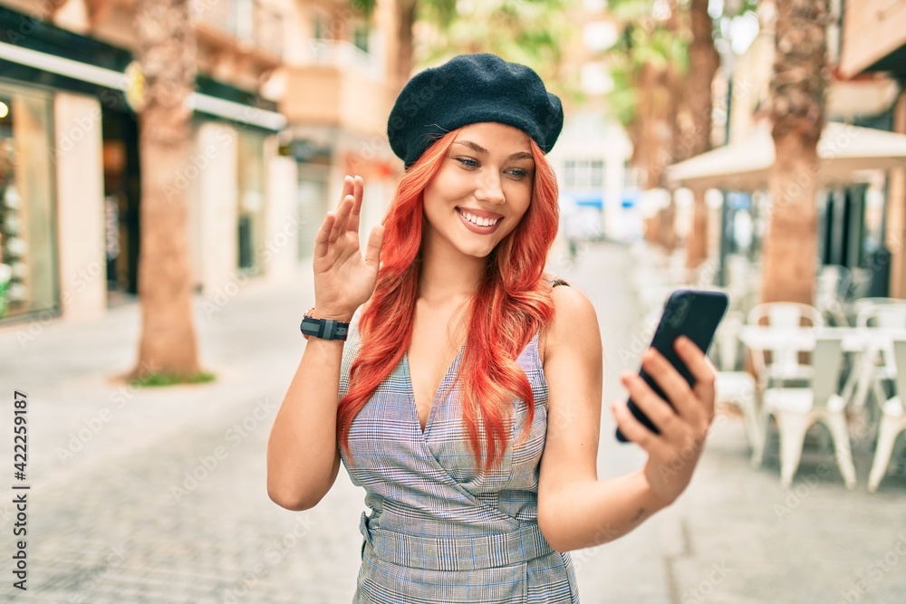 Young redhead girl wearing french style doing video call using smartphone at the city.