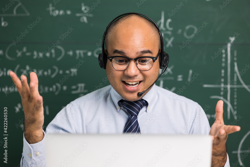 Indian young teacher man sitting wearing headset teaching online video conference live stream by laptop. Asian teacher teaching mathematics class webinar online for students learning.