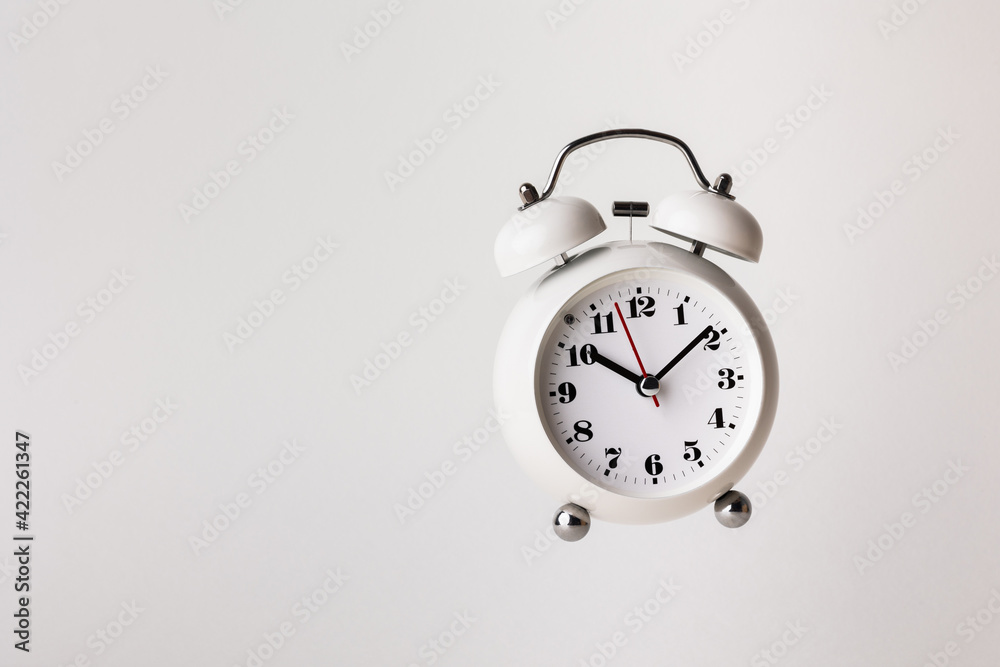 Small white alarm clock, black numbers, set the time for 10.10 o'clock, placed on a white table. Small white alarm clock, black numbers, set the time for 10.10 o'clock, placed on a white table.